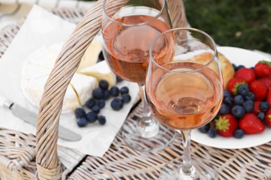 Glasses of delicious rose wine and food on picnic basket outdoors, closeup