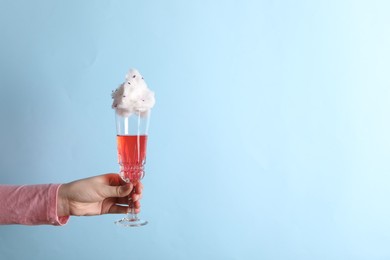 Woman holding glass of cotton candy cocktail on light blue background, closeup. Space for text