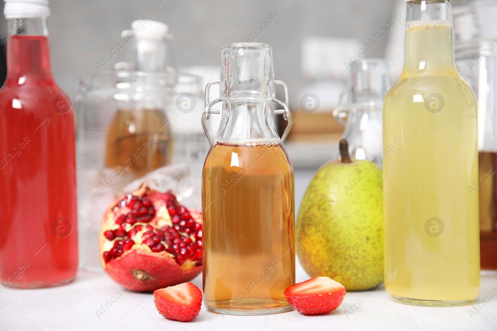 Photo of Tasty kombucha in glass bottles and fresh fruits on white tiled table