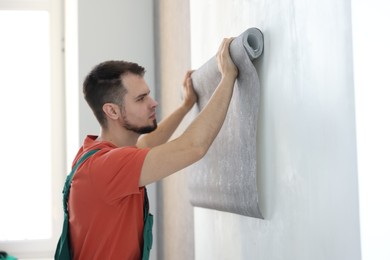 Man hanging stylish gray wallpaper in room