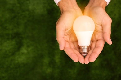 Photo of Man holding lamp bulb against green background, top view. Space for text
