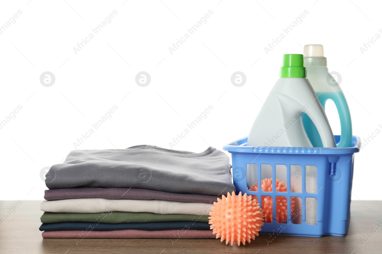 Photo of Orange dryer balls, laundry detergents and stacked clean clothes on wooden table against white background