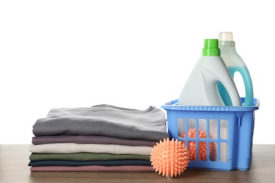 Photo of Orange dryer balls, laundry detergents and stacked clean clothes on wooden table against white background
