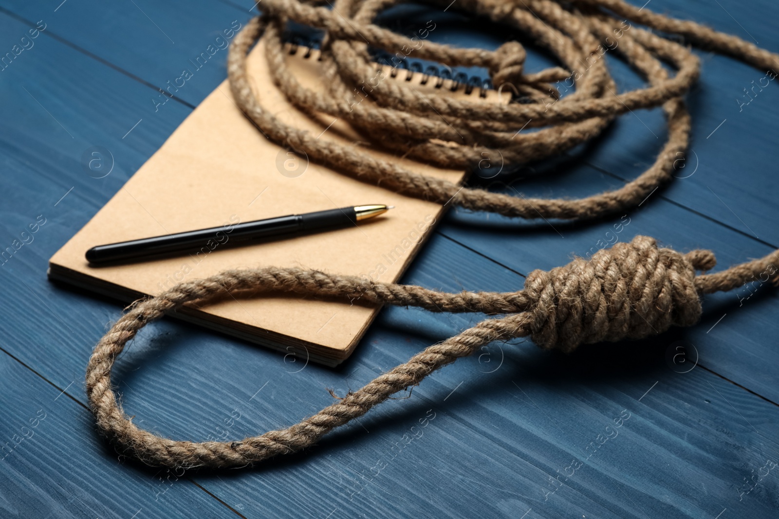 Photo of Rope noose and blank notebook with pen on blue wooden table, closeup