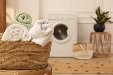 Photo of Basket with clean rolled towels on stool in laundry room. Space for text