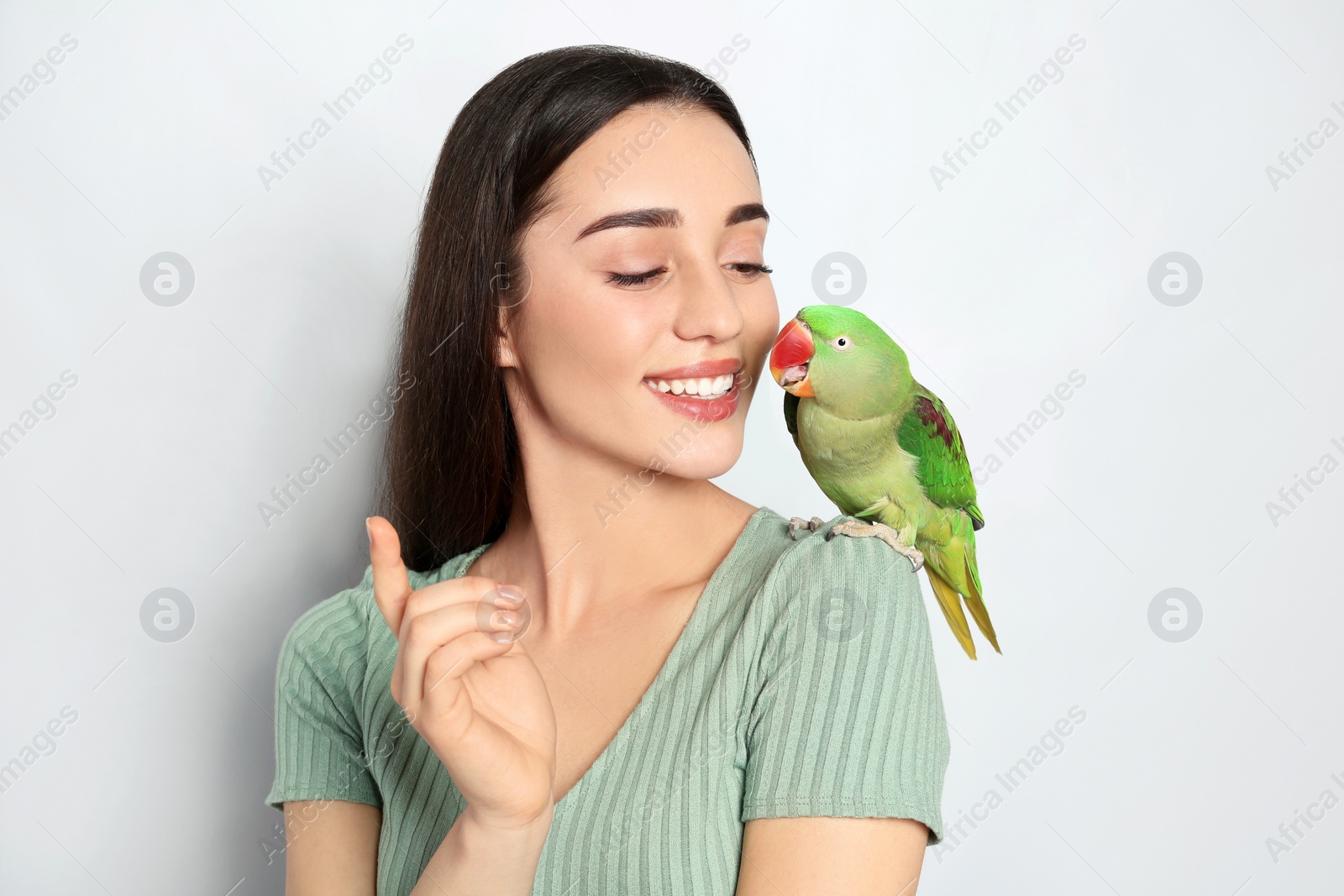 Photo of Young woman with Alexandrine parakeet on light background. Cute pet