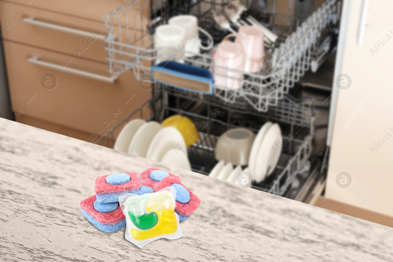 Image of Dishwasher detergent pod and tablets on white wooden table in kitchen