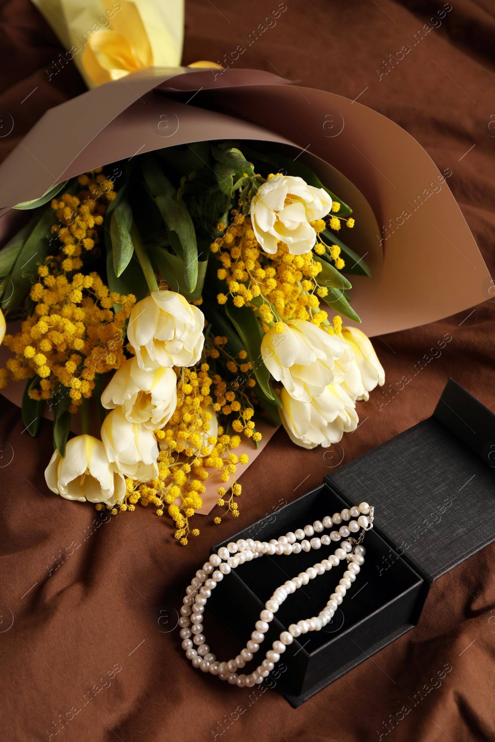 Photo of Bouquet of beautiful spring flowers and necklace on brown fabric, above view