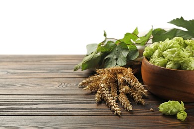 Photo of Fresh hop flowers and wheat ears on wooden table against white background, space for text