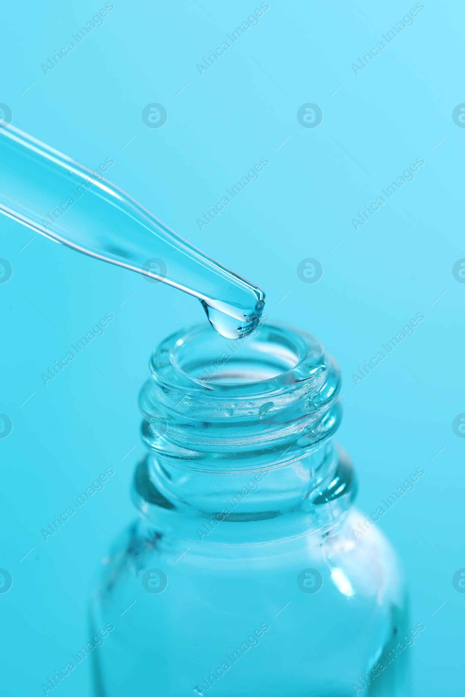 Photo of Dripping liquid from pipette into glass bottle on light blue background, closeup