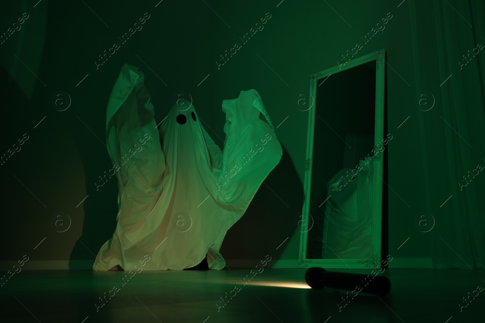 Photo of Creepy ghost. Woman covered with sheet near mirror in green light