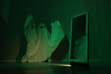 Photo of Creepy ghost. Woman covered with sheet near mirror in green light
