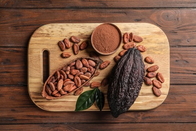 Photo of Board with cocoa pods, beans and powder on wooden table, top view