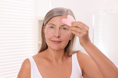 Photo of Woman massaging her face with rose quartz gua sha tool in bathroom