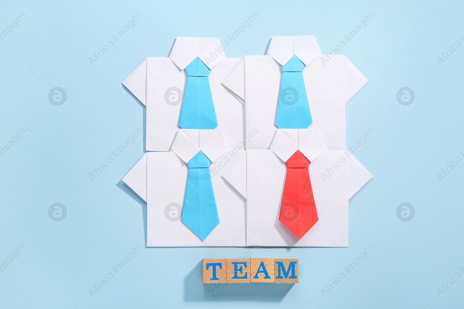 Photo of Many paper shirts and word Team on light blue background, flat lay. Recruiter searching employee