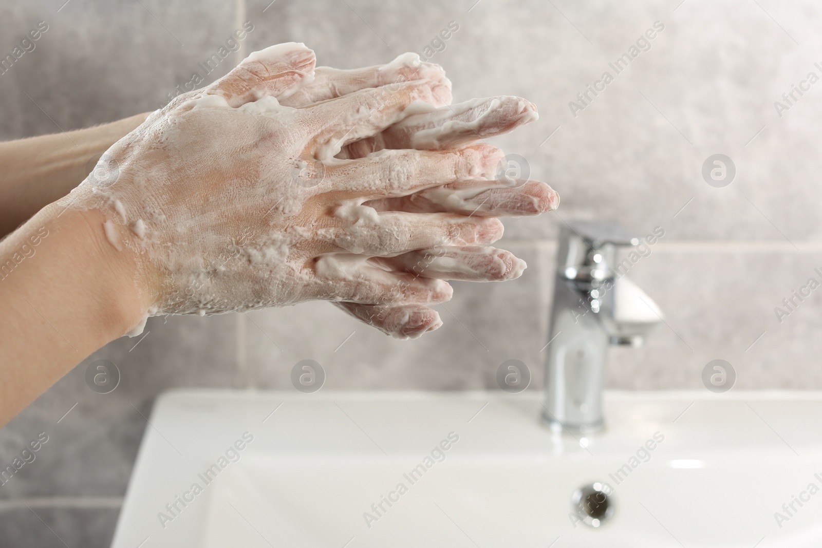 Photo of Woman washing hands with cleansing foam near sink in bathroom, closeup