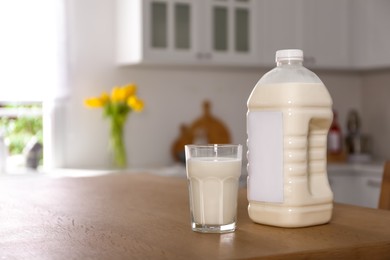 Photo of Gallon bottle of milk and glass on wooden table in kitchen. Space for text