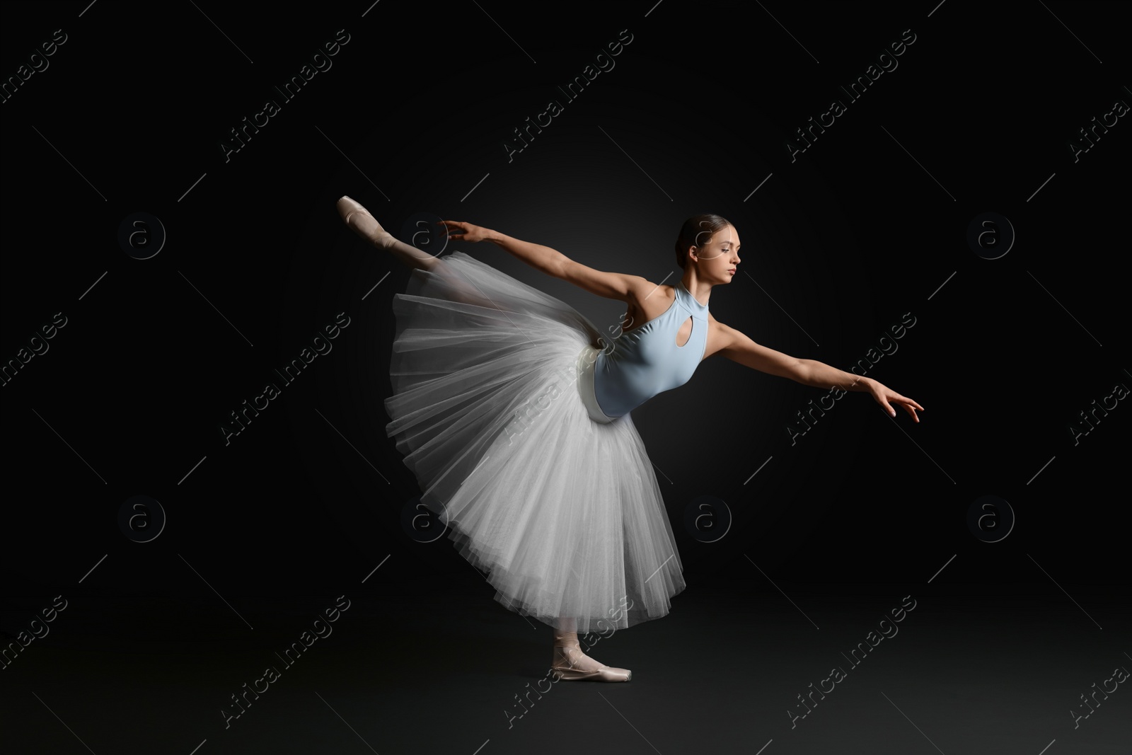 Photo of Young ballerina practicing dance moves on black background