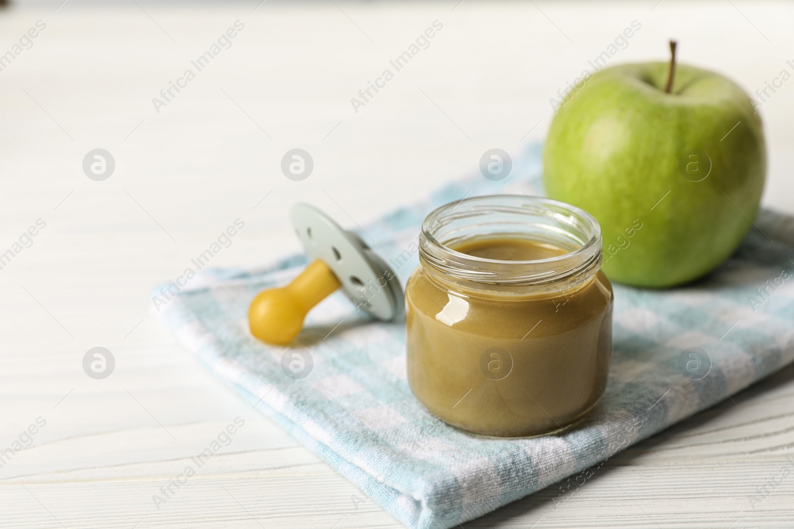 Photo of Jar with healthy baby food, apple and pacifier on white wooden table. Space for text