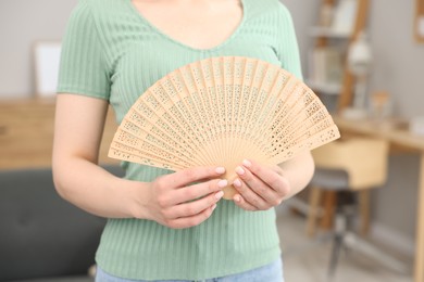 Woman with hand fan at home, closeup