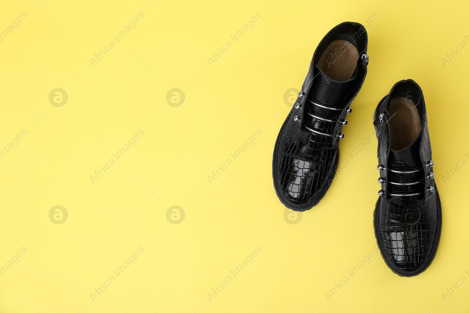 Photo of Pair of stylish ankle boots on yellow background, top view. Space for text