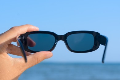 Photo of Woman holding stylish sunglasses near sea, closeup