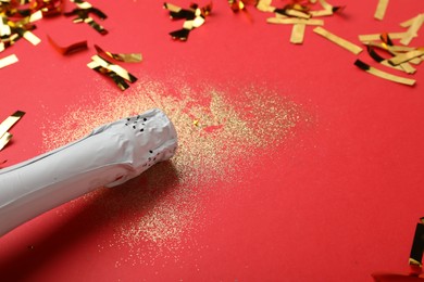 Photo of Composition with shiny glitters, champagne bottle and confetti on red background, closeup