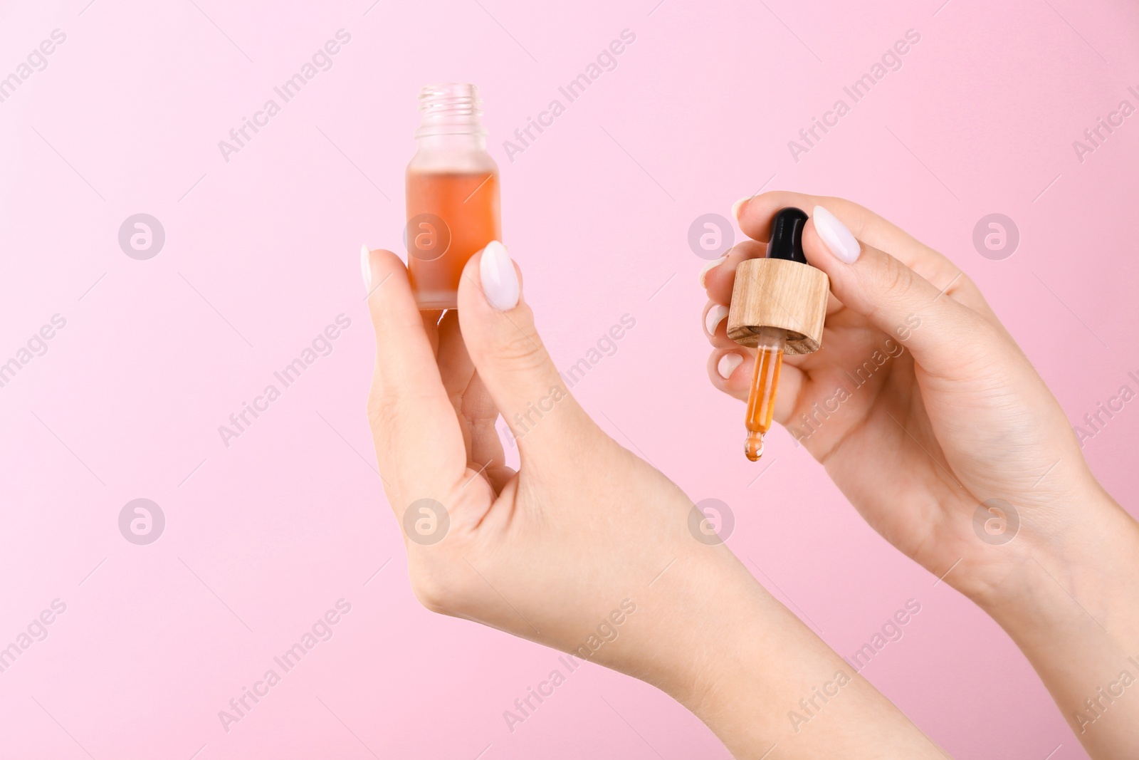 Photo of Woman applying essential oil onto wrist against pink background, closeup