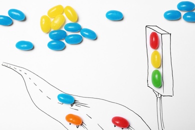 Photo of Colorful jelly candies arranged as traffic light and road with cars on white background, top view