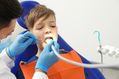 Photo of Professional dentist working with little boy in clinic. Space for text