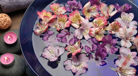 Photo of Bowl of water with flowers, candles and stones on table, closeup. Spa treatment