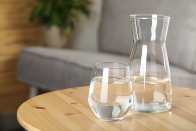 Photo of Jug and glass of water on wooden table in room, space for text. Refreshing drink