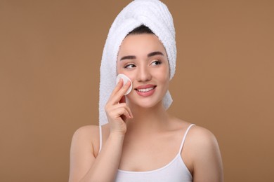 Photo of Beautiful woman in terry towel removing makeup with cotton pad on beige background