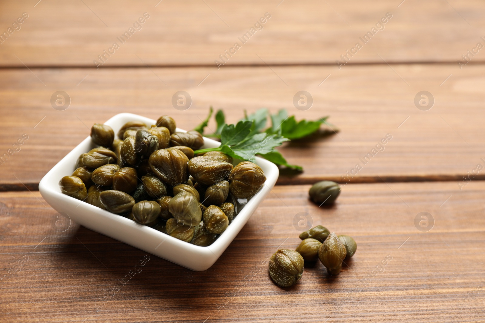 Photo of Tasty capers and parsley on wooden table, space for text