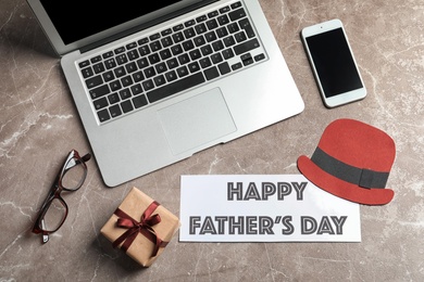 Photo of Smartphone, laptop, gift box and card with words HAPPY FATHER'S DAY on grey background, top view