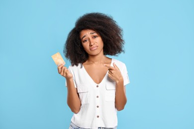 Photo of Confused woman pointing at credit card on light blue background. Debt problem