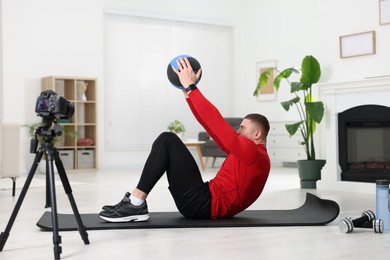 Photo of Trainer with ball recording workout on camera at home