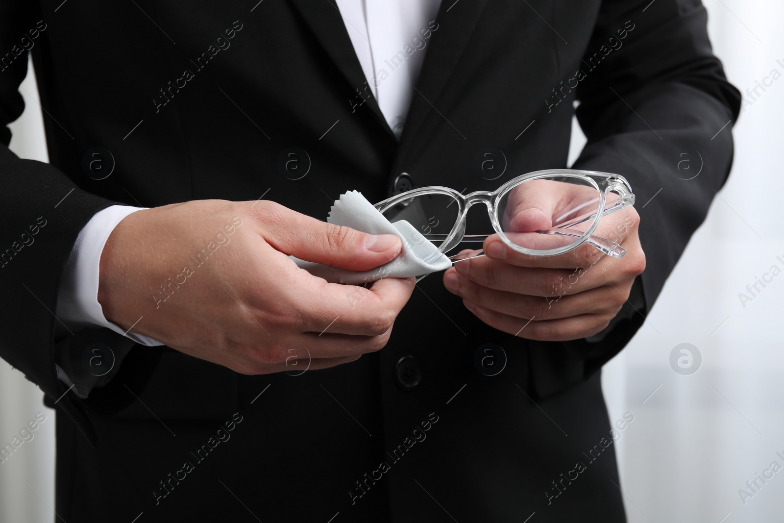 Photo of Man wiping glasses with microfiber cloth indoors, closeup