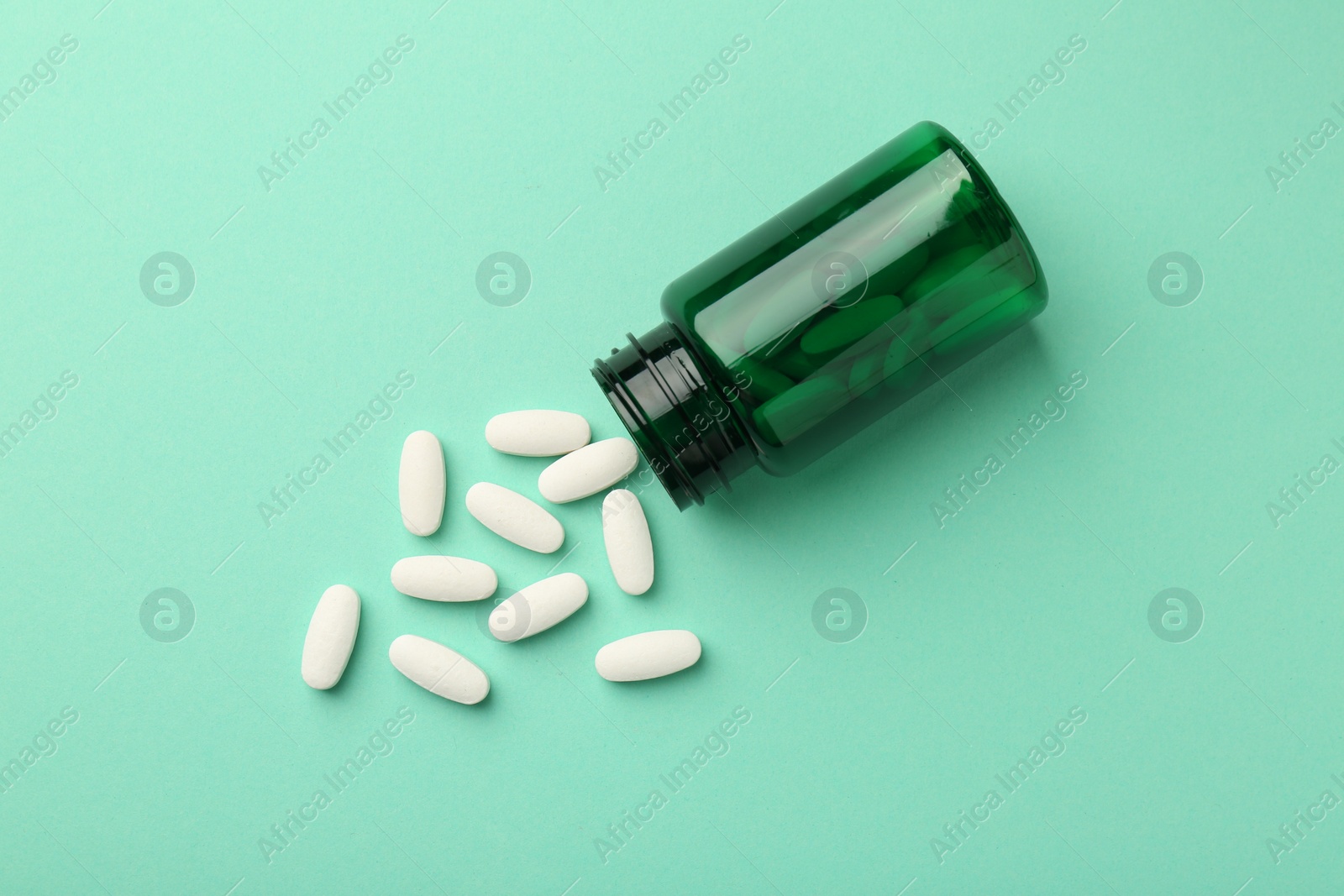 Photo of Vitamin pills and bottle on mint color background, top view