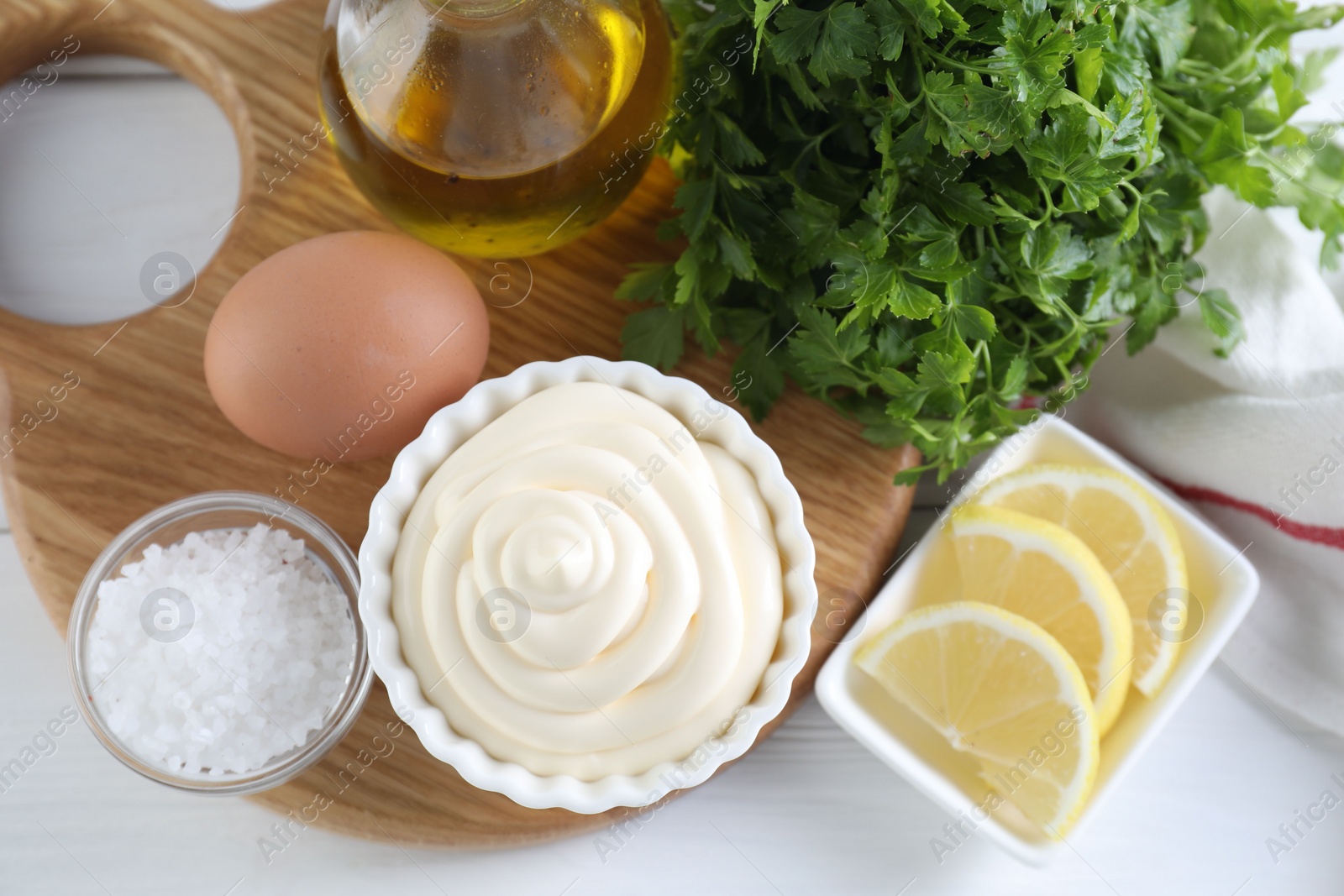 Photo of Fresh mayonnaise sauce in bowl and ingredients on white wooden table, flat lay