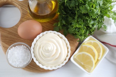 Fresh mayonnaise sauce in bowl and ingredients on white wooden table, flat lay