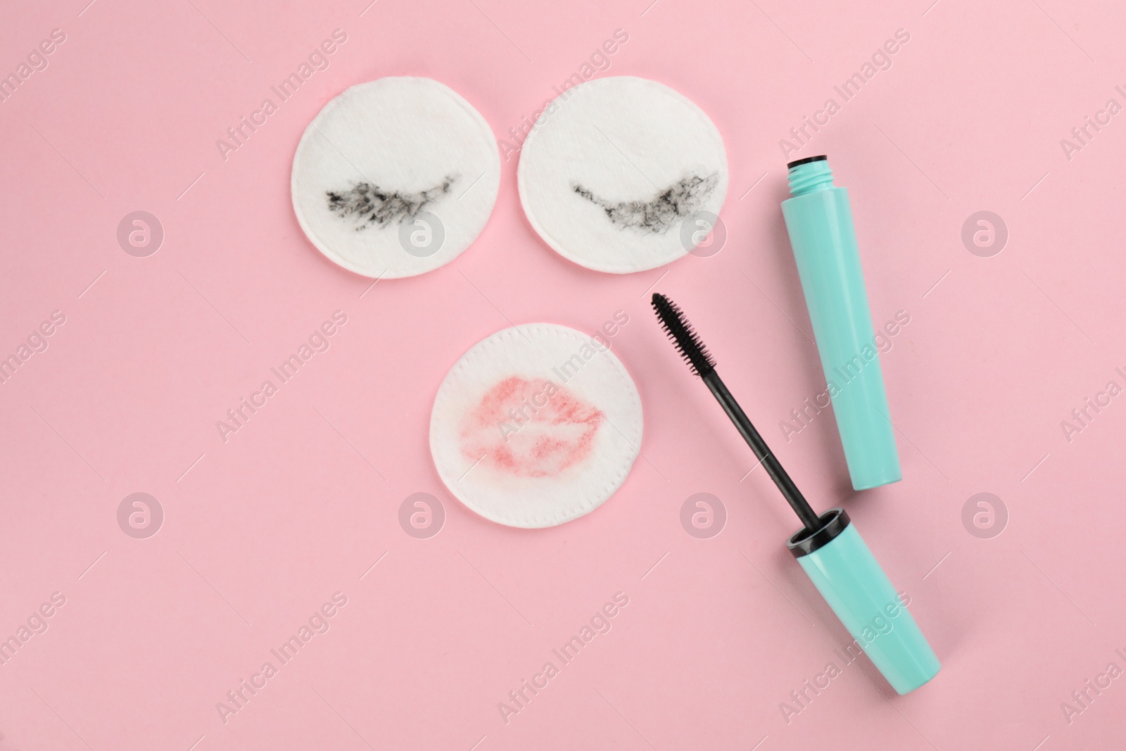 Photo of Dirty cotton pads and mascara on light pink background, flat lay