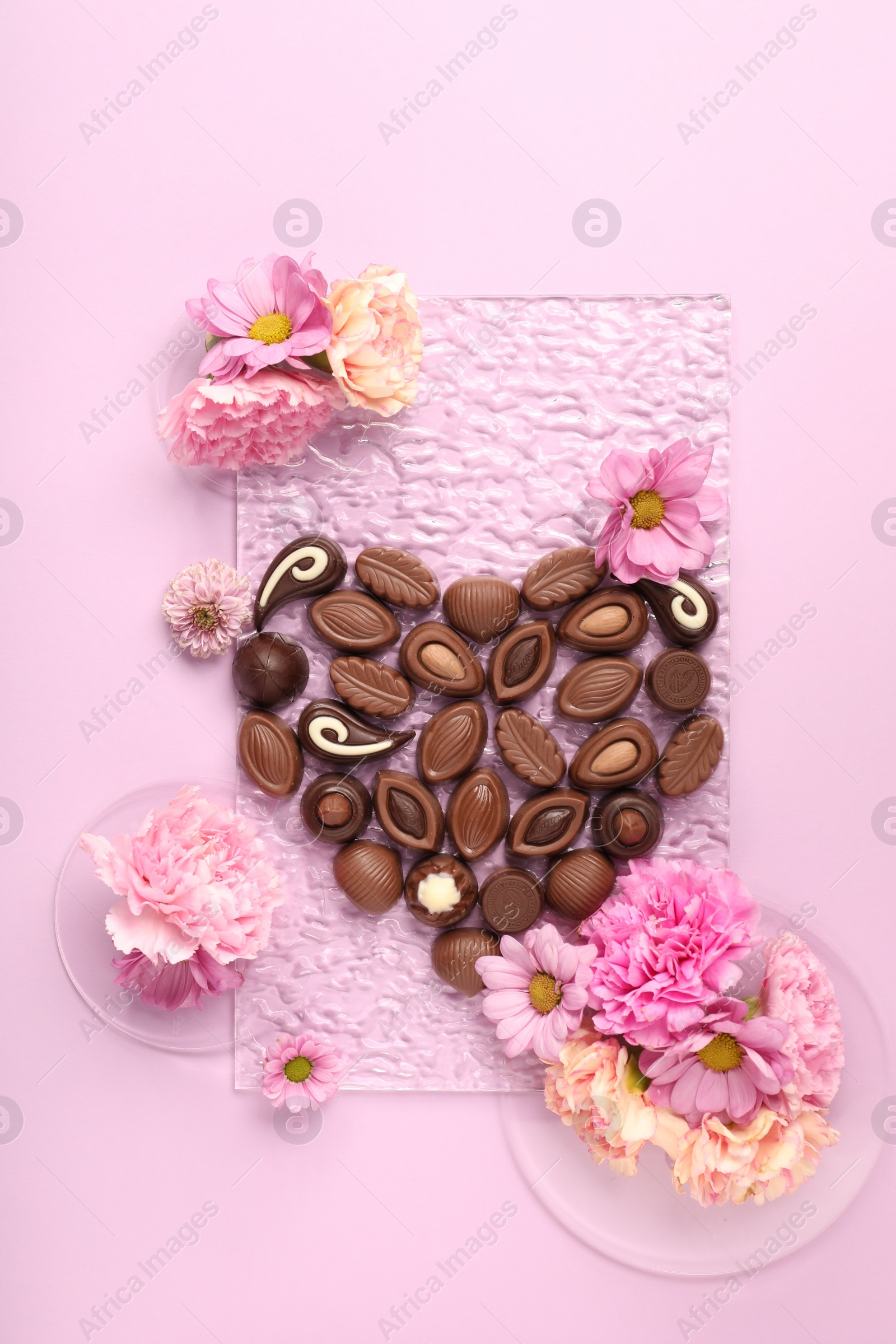 Photo of Heart made with delicious chocolate candies and beautiful flowers on pink background, flat lay