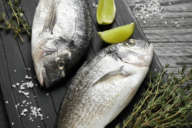 Raw dorada fish on black wooden table, closeup