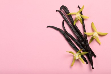Photo of Vanilla pods and beautiful flowers on pink background, top view. Space for text