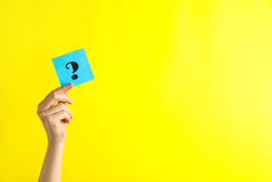 Woman holding note with question mark on yellow background, closeup. Space for text