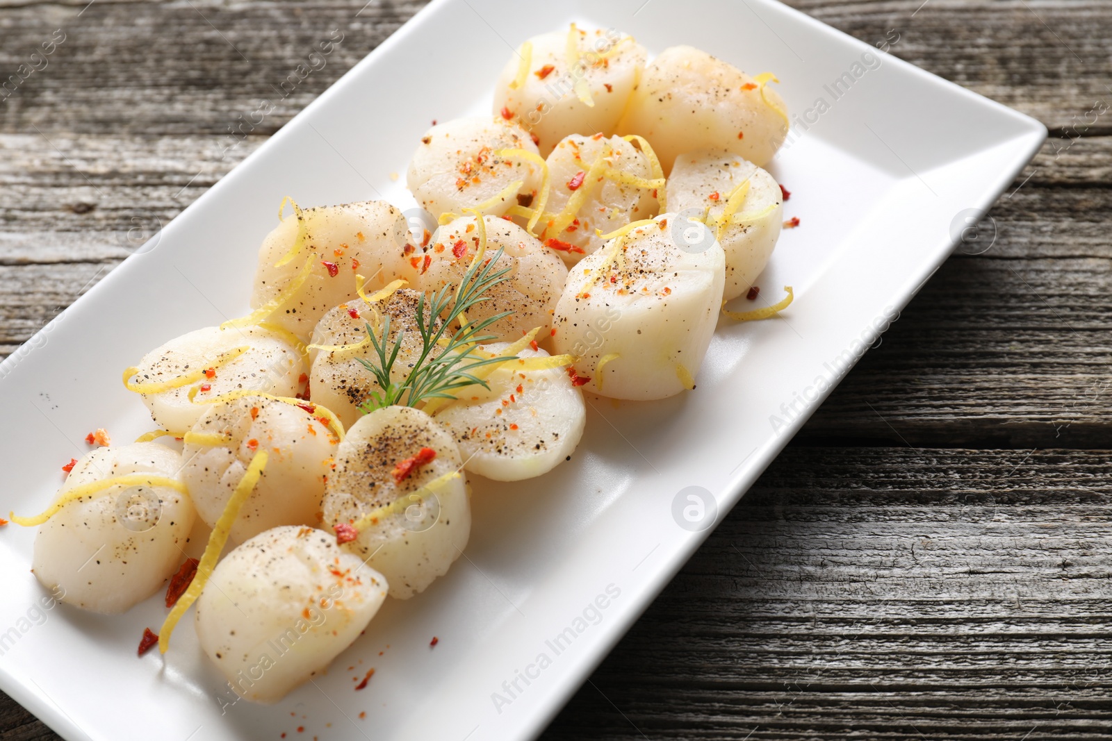 Photo of Raw scallops with spices, dill and lemon zest on wooden table, closeup