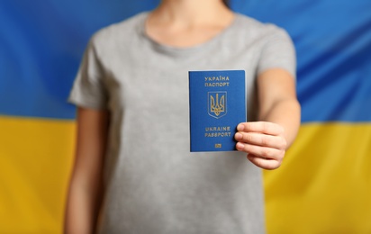 Photo of Woman holding Ukrainian travel passport against national flag, closeup with space for text. International relationships