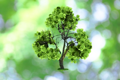 Tree with green leaves in shape of recycling symbol on blurred background. Bokeh effect