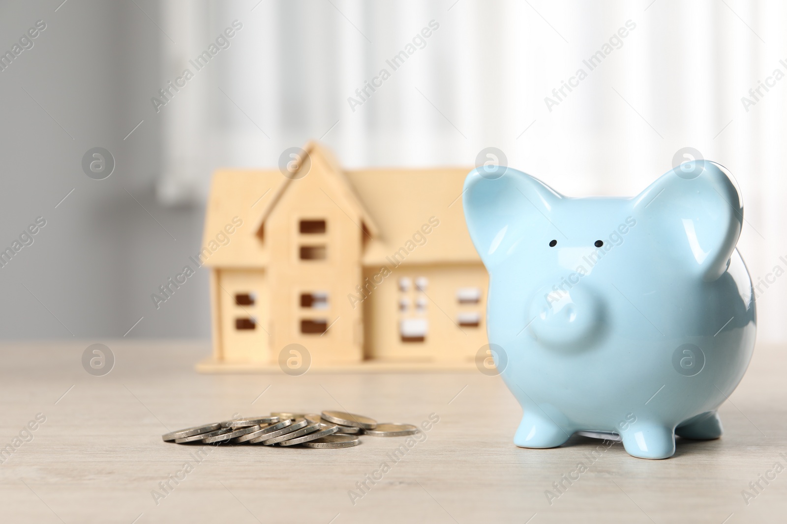 Photo of House model, piggy bank and coins on wooden table indoors, selective focus